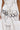 Only the lower torso and hand are visible as a person wears a white dress with black stitching, metallic studs, and the TEST MY LUCK HORSESHOE BELT featuring black and silver horseshoe pendants.