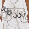 Only the lower torso and hand are visible as a person wears a white dress with black stitching, metallic studs, and the TEST MY LUCK HORSESHOE BELT featuring black and silver horseshoe pendants.