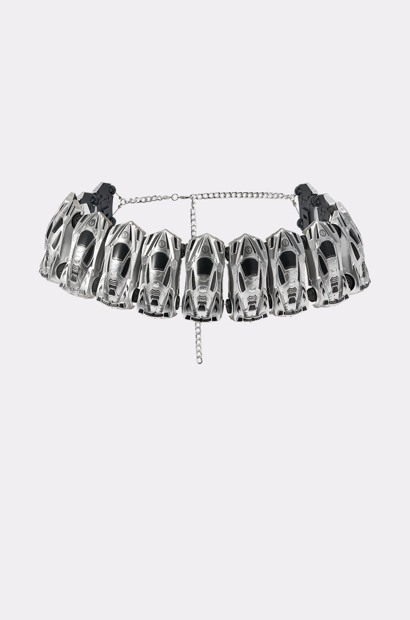 The VROOM VROOM CAR BELT, a silver choker with a chrome finish and black accents, is crafted from connected miniature car models and has an adjustable chain. Styled with Y2K vibes, it's shown against a plain white background. 4