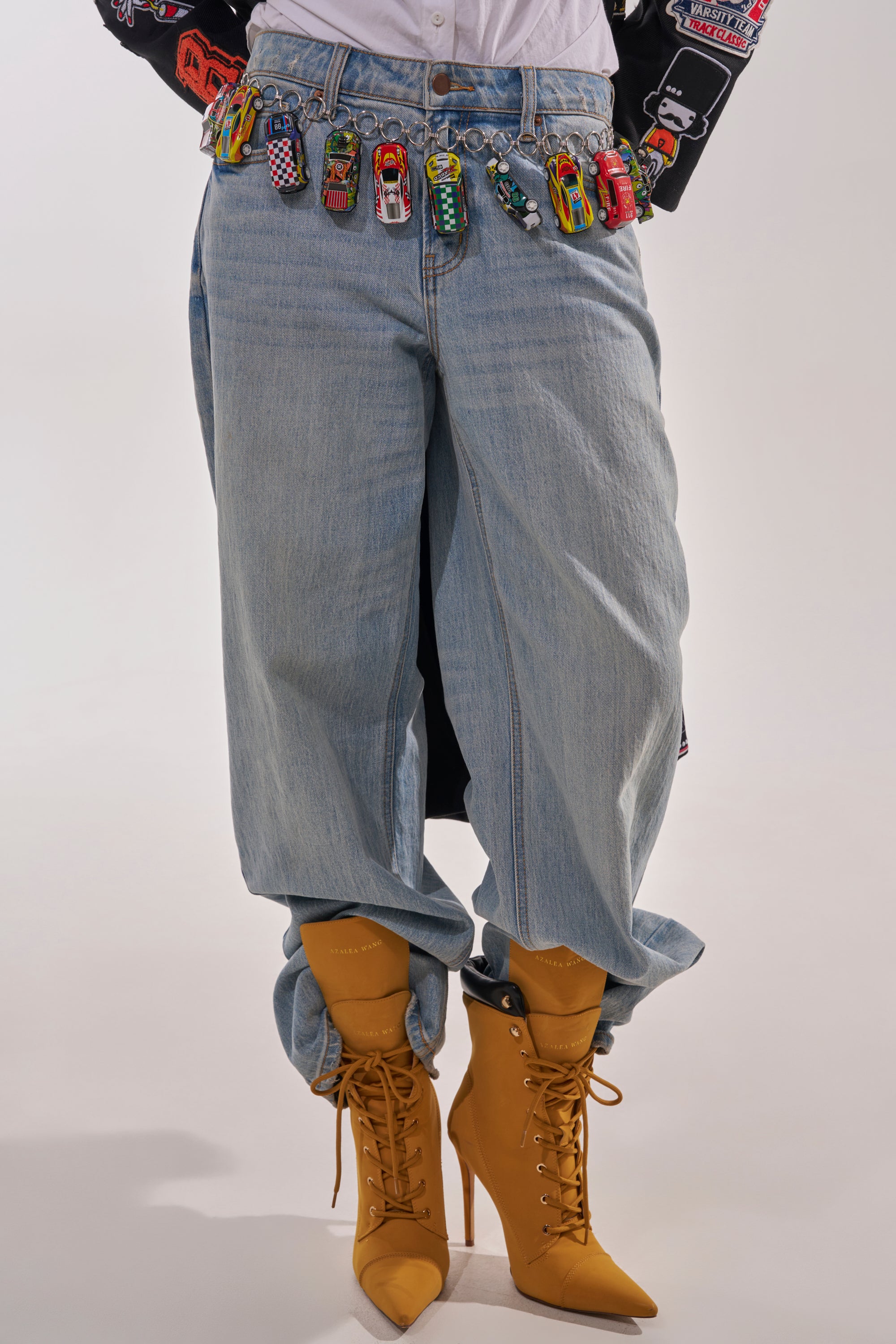 Person wears baggy light blue jeans, a white shirt, mustard yellow lace-up high-heeled boots, and a VROOM CAR CHAIN BELT around the waist. Only the lower half of the body is shown. 1