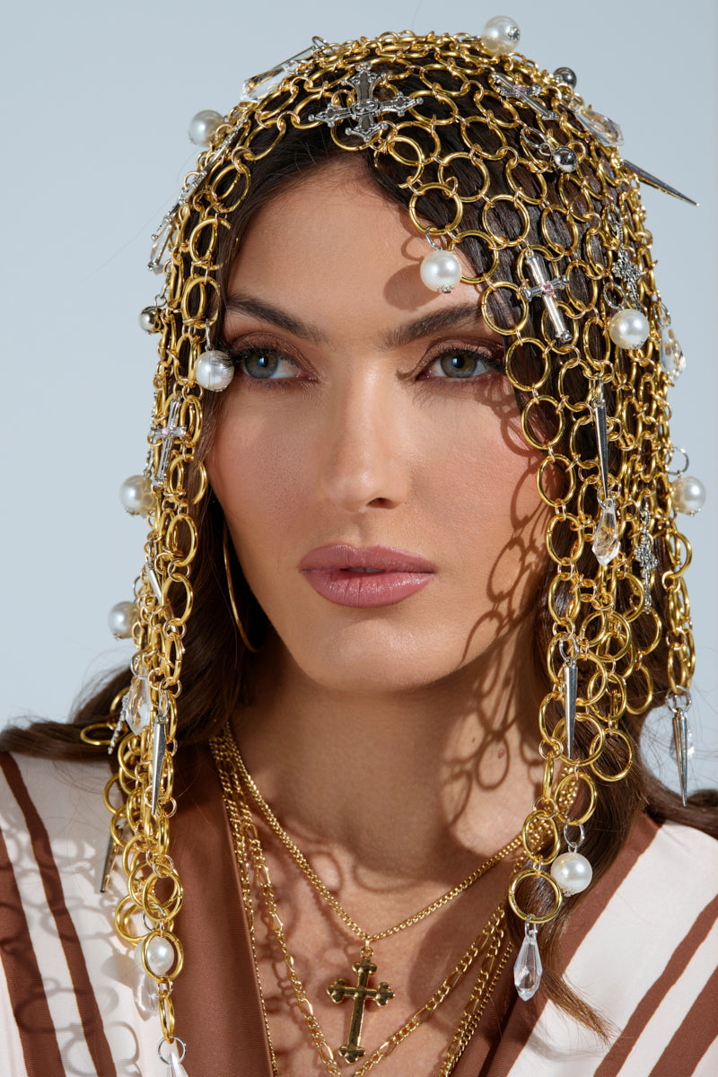 A person with long hair is wearing the ALWAYS BLESSED HEADPIECE, adorned with pearl embellishments and crystal beads. They accessorize with hoop earrings, layered necklaces, and a cross pendant against a neutral light backdrop. 1