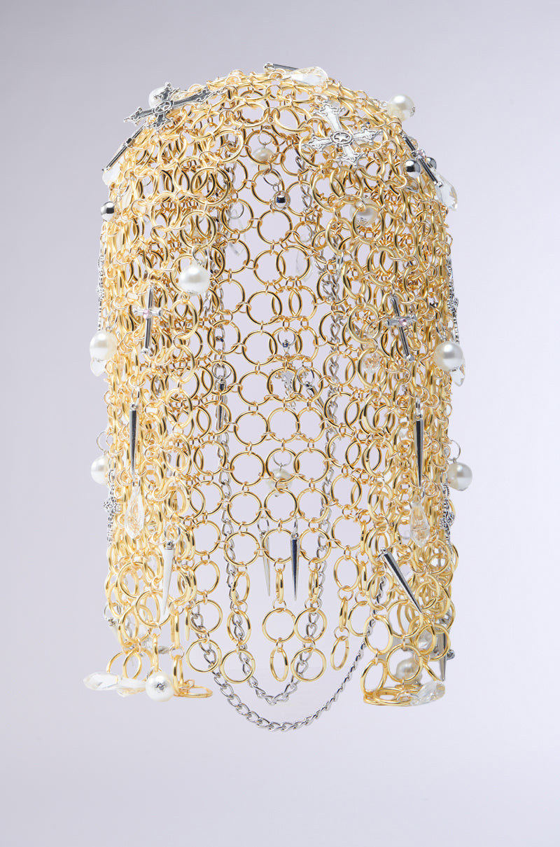 The ALWAYS BLESSED HEADPIECE features elaborate gold rings adorned with pearl embellishments and silver spikes. Silver chain links and decorative elements further enhance the accessory, offering a striking contrast against the gold and pearls. 5