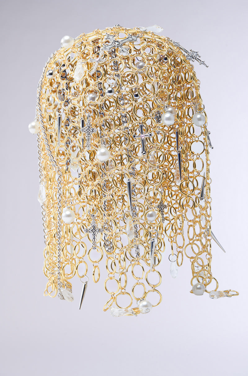 The ALWAYS BLESSED HEADPIECE features a gold chain headdress with pearl embellishments, crystals, and silver spikes. Its cascading design forms an elegant pattern, blending textures and reflective elements beautifully against a neutral background. 3