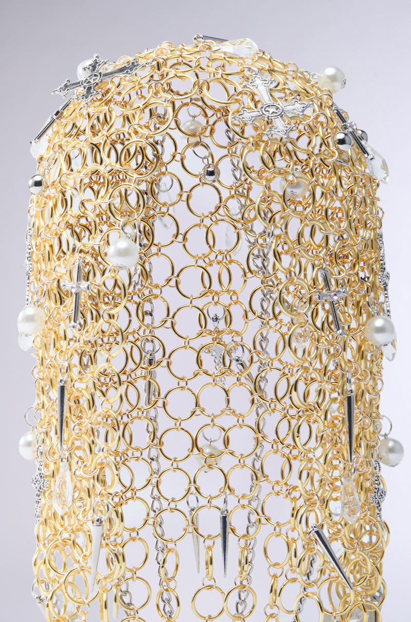 The ALWAYS BLESSED HEADPIECE features gold rings and silver chain links, adorned with pearl embellishments, silver crosses, and spike pendants. Its intricate design boasts layered loops and decorative elements set against a plain gray background. 4
