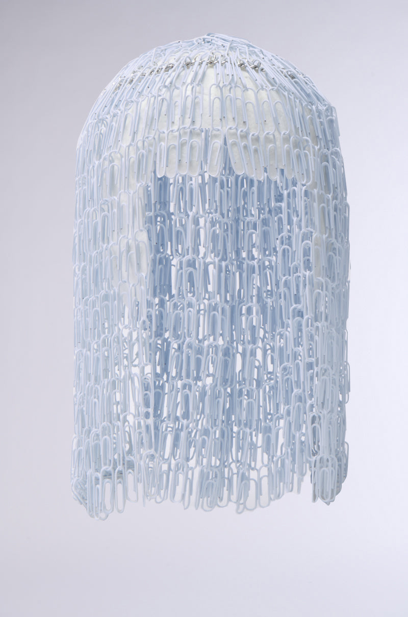 The IN YOUR DREAMS CLIP HAIR PIECE features cascading chains of interlinked white paper clips draped over a helmet-like base, creating a striking metallic fringe effect against a light, plain background.