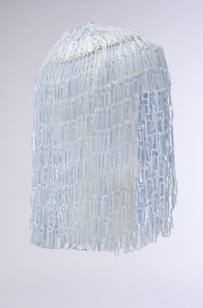 The IN YOUR DREAMS CLIP HAIR PIECE drapes interlinked white paperclips over a white head-shaped form, creating a metallic fringe veil that cascades from the top and obscures the face, set against a light grey background.