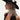 Embodying queen sh*t vibes, a person dons the QUEEN SH*T BLING HEADPIECE—a black wide-brimmed hat adorned with silver rhinestones and floral decorations. In all black, tattoos peek from their arm as they gaze sideways against a light backdrop, exuding striking elegance.