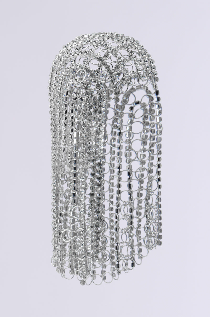 The QUEEN SH*T BLING HEADPIECE features an arrangement of interlinked silver rings that form a head-shaped sculpture, similar to chainmail. Its gleaming surface lends an intricate and delicate pattern, evocative of an ornate headpiece. It is displayed against a plain, light gray background.
