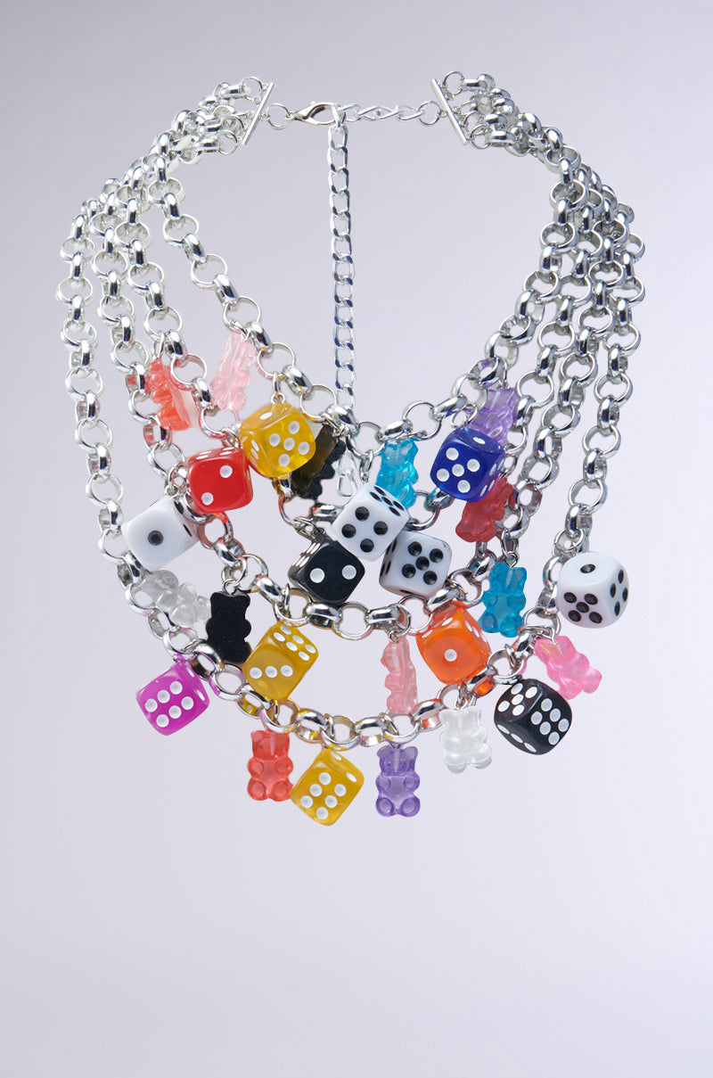 The ROLL THE DICE CHARM CHOKER showcases vibrant silver chains decorated with multicolored dice and gummy bear charms—red, blue, black, white, and orange. It features an adjustable clasp for versatile styling against a plain background.