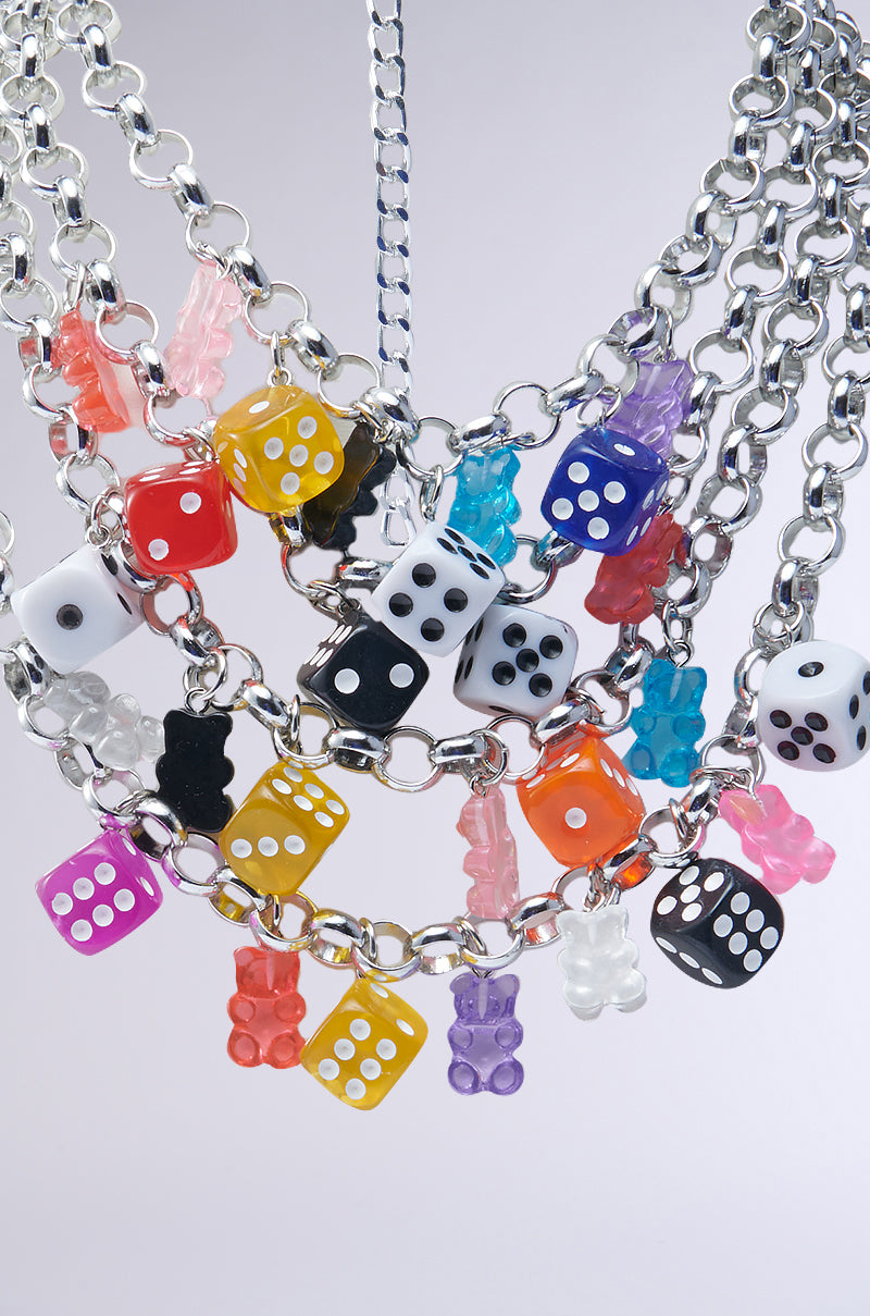 Explore the AKIRA Label's ROLL THE DICE CHARM CHOKER, boasting silver chains with colorful dice and gummy bear pendants. The dice feature vibrant colors like yellow, pink, blue, and black with unique dots, while the gummy bears are equally captivating in their diverse hues.