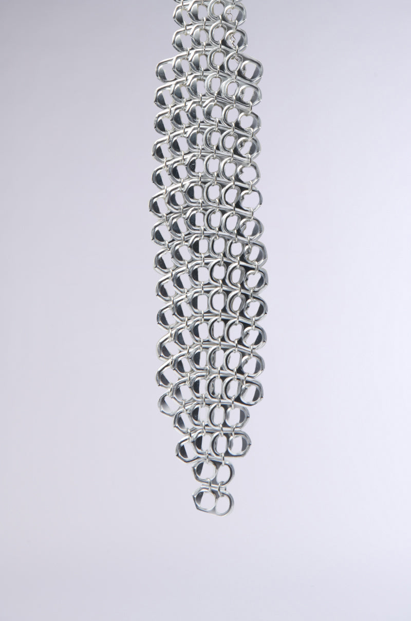 The STAY POPPIN TIE features interlinked faux silver pop can tabs in a vertical arrangement on a light gray backdrop. Its sculptural silhouette forms a zigzag pattern that cascades downwards, offering an industrial-chic vibe. 2