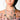 A woman with blue eyes and glossy lips wears large hoop earrings and the CROSS MY HEART SILVER NECKLACE, layered with crystal crosses and religious medals. Her manicured nails and floral off-the-shoulder top add a gothic glam touch.