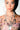 A woman with blue eyes and glossy lips wears large hoop earrings and the CROSS MY HEART SILVER NECKLACE, layered with crystal crosses and religious medals. Her manicured nails and floral off-the-shoulder top add a gothic glam touch.