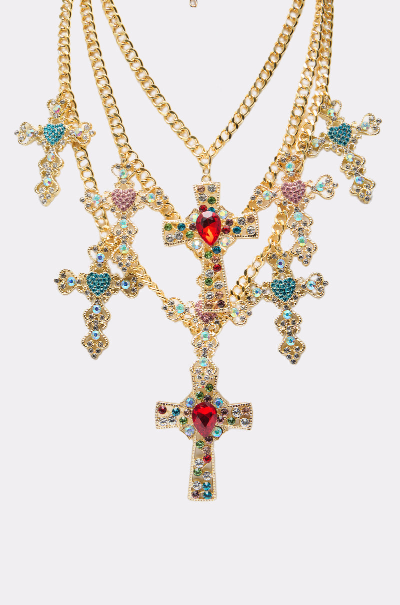 The IN MY FEELINGS NECKLACE features five bold cross pendants with ornate gold chains and vibrant red, blue, and pink gemstones, beautifully displayed on a white background—a perfect statement piece for any occasion.