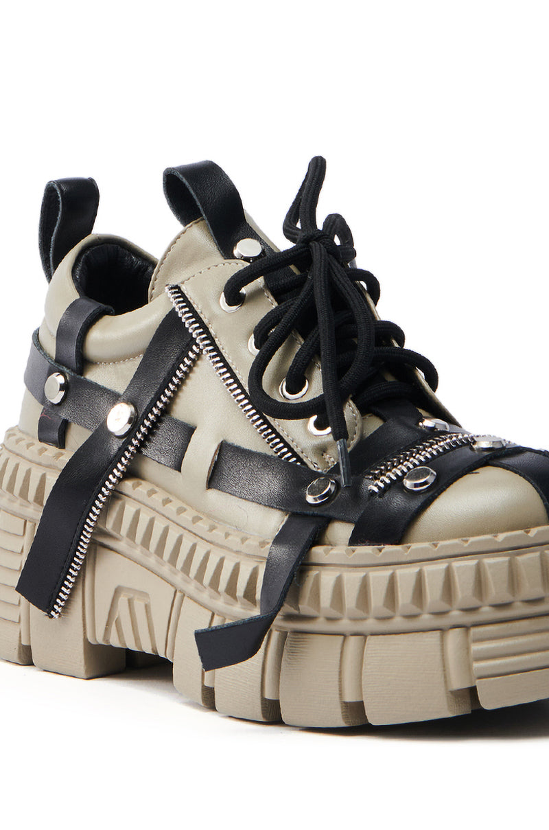 The AZALEA WANG BEAGLE KHAKI FLAT SNEAKER is a chunky beige sneaker featuring black faux leather straps, silver rivets, zippers, thick flatform lug soles, and black laces for a rugged, edgy design.