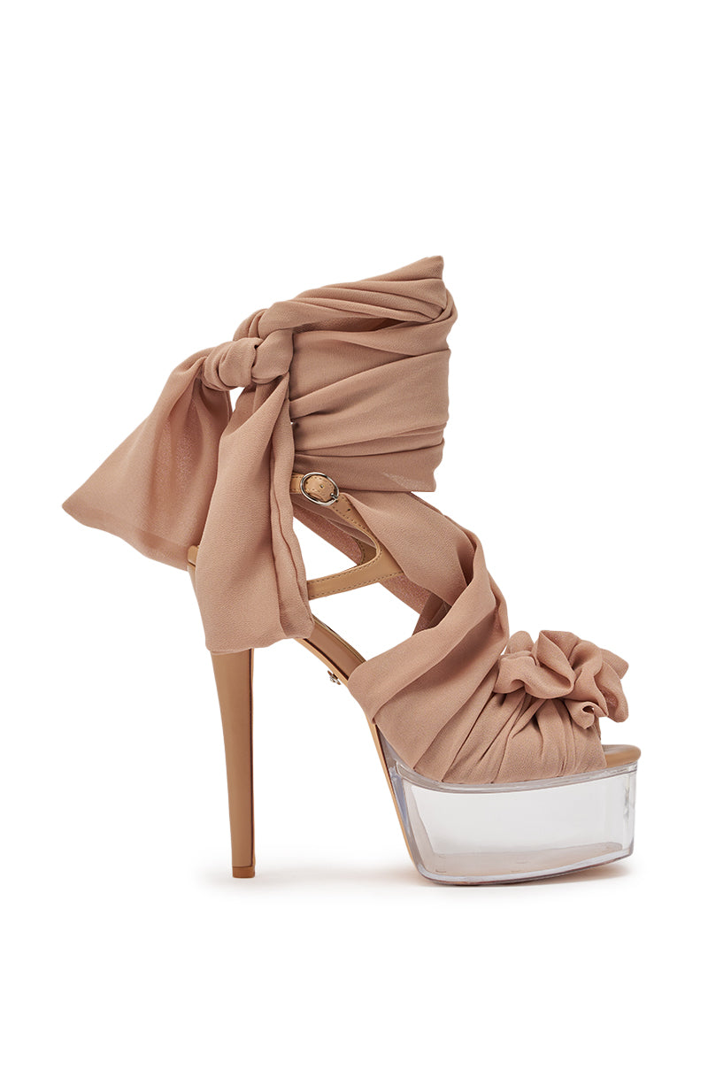 The AKIRA GOLD BEAUDEN TAN PLATFORM TIE SANDAL features a high stiletto clear platform, beige heel, and soft nude fabric straps that wrap around the ankle and foot, tied in decorative knots and bows. 4