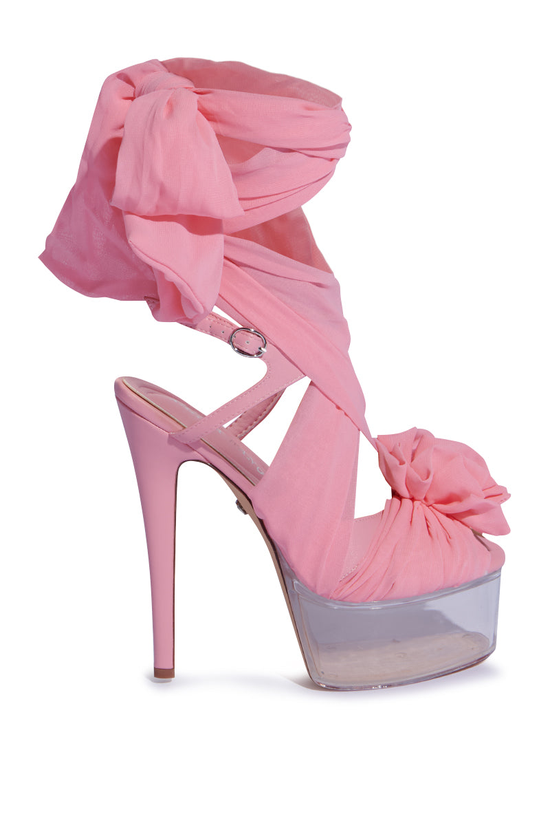 The AZALEA WANG BEAUDEN PINK STILETTO SANDAL elegantly wraps around the ankle with a ruffled chiffon and features a large bow. It has pink heels and platforms with clear bases, creating a stylish look for any occasion.
