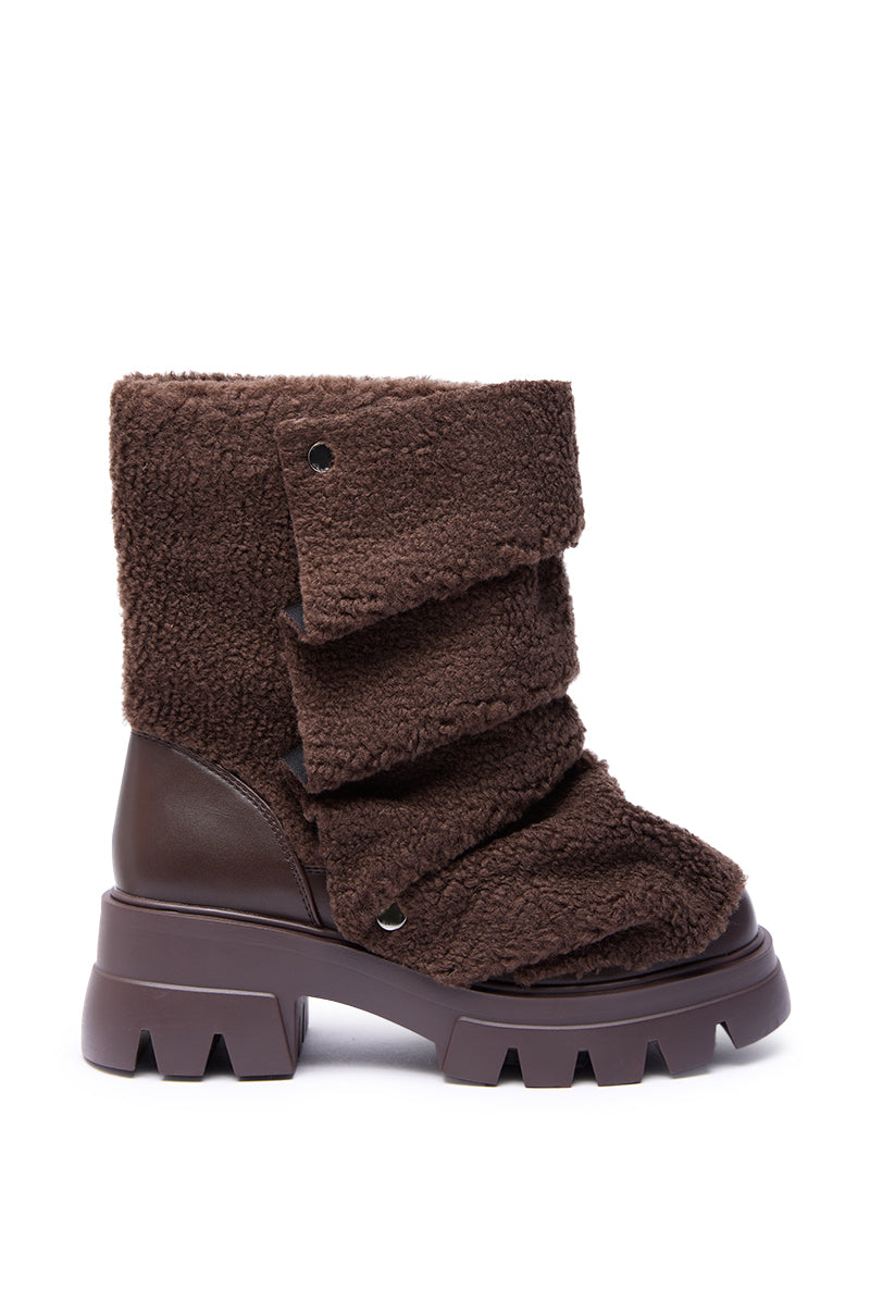 The AZALEA WANG BEHATI BROWN SHERPA BOOTIE WITH SNAP DETAIL features a chunky sole, fleece-like textured upper, layered flaps with snap buttons, and faux leather heel and lower section for a rugged yet stylish look.