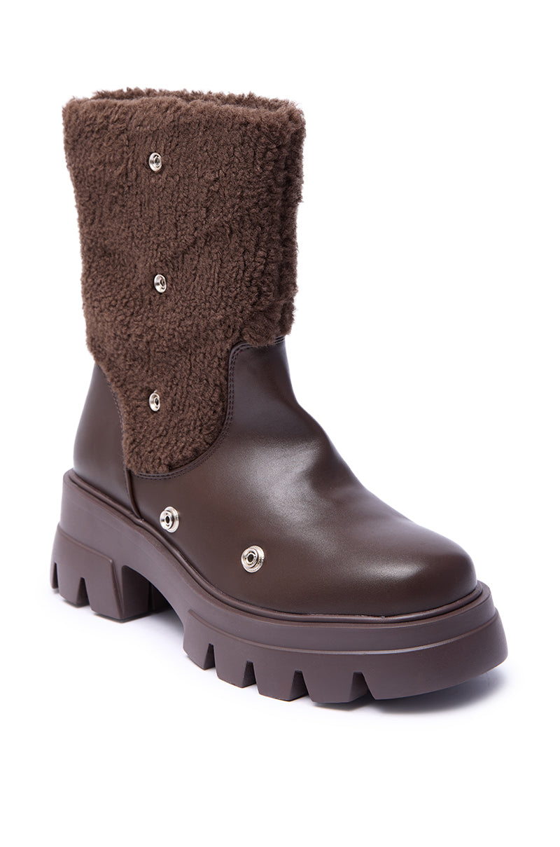 The AZALEA WANG BEHATI BROWN SHERPA BOOTIE WITH SNAP DETAIL features a chunky sole, smooth leather foot, and a faux sherpa upper shaft accented with metal snap details.