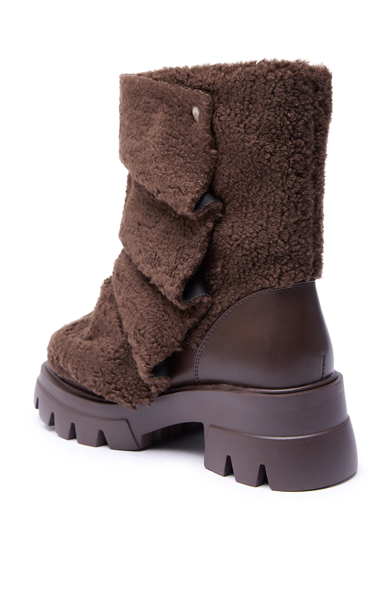 The AZALEA WANG BEHATI Brown Sherpa Bootie features chunky textured shearling, a thick lug sole, layered flaps, snap detail, and smooth leather accents on the heel and midsole.