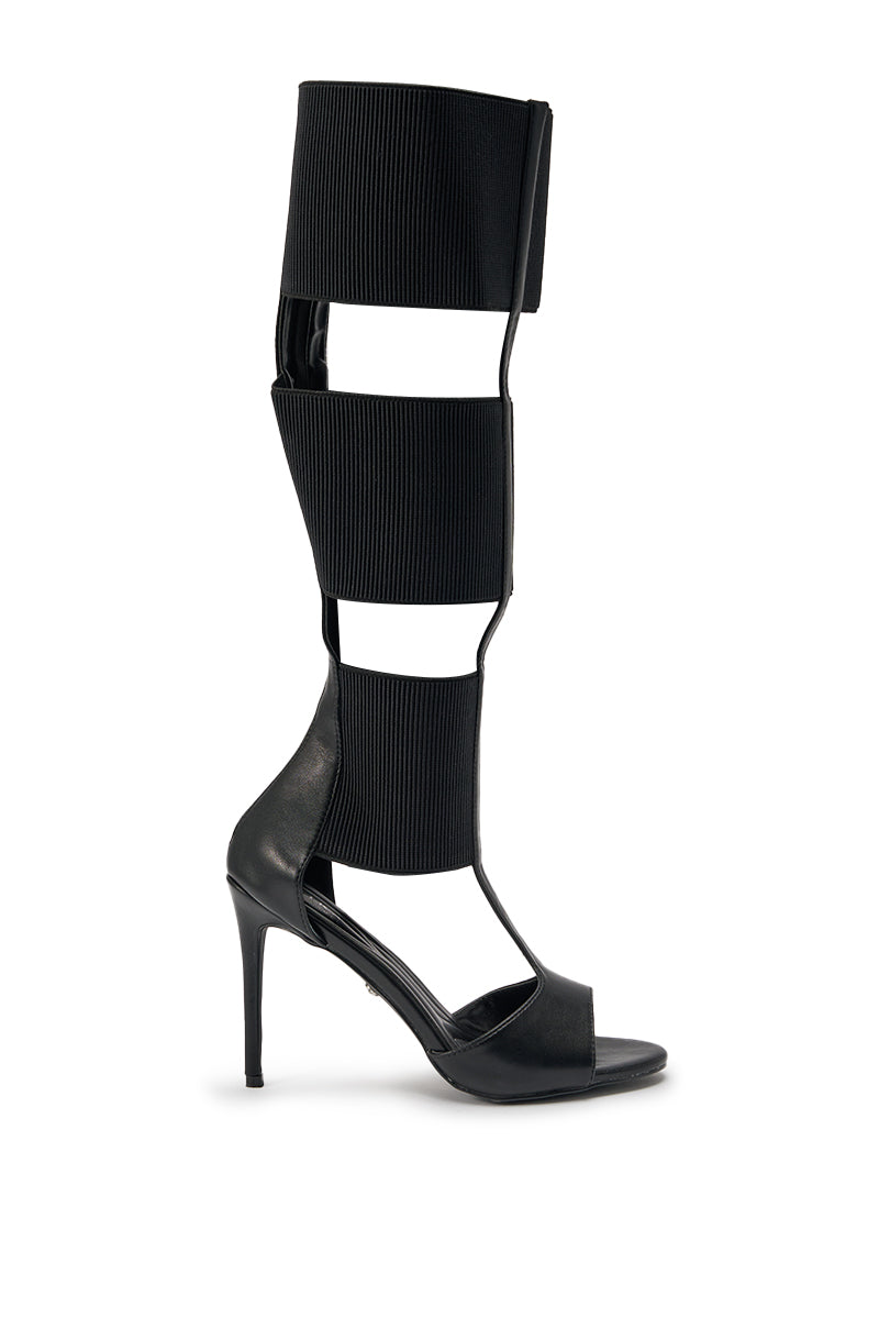 The AKIRA GOLD BELLANTRA BLACK GLADIATOR STILETTO SANDAL is a modern open-toe, black high heel with three ribbed elastic straps up the calf, sleek faux leather accents, and a striking stiletto heel. 3