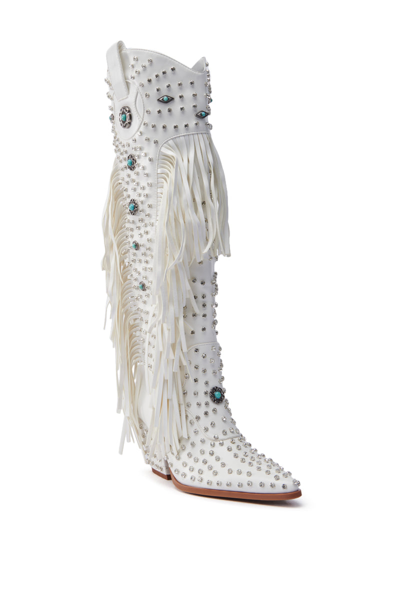 The AZALEA WANG BENNETT WHITE BOOT is a knee-high cowgirl boot in faux leather with silver studs, turquoise gemstones, and long side fringes. It features a pointed toe and high heel for a stylish statement.