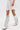 A person stands against a plain white background wearing a white fringed skirt and the AZALEA WANG BENNETTO SILVER RHINESTONE WESTERN BOOT, featuring sparkly silver rhinestones and fringe. A colorful thigh tattoo is visible.