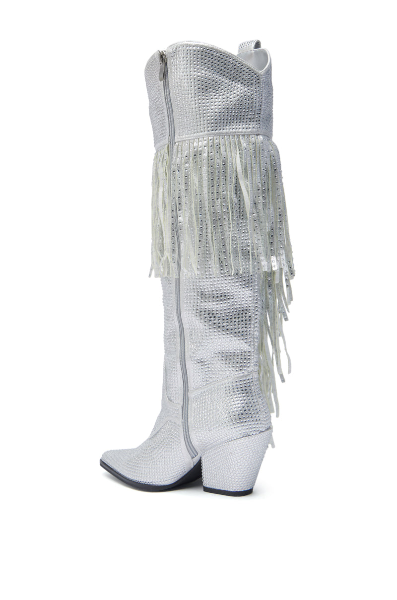 The AZALEA WANG BENNETTO SILVER RHINESTONE WESTERN BOOT features a tall silhouette, pointed toe, mid-height angled heel, side zipper, and decorative white fringe around the upper shaft.