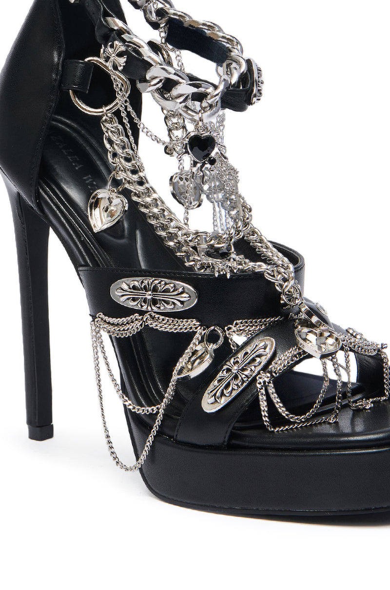 The AZALEA WANG BEREN BLACK HARDWARE EMBELLISHED SANDAL is a black faux leather platform stiletto adorned with silver chains and metallic charms across the straps for a striking decorative look. 4