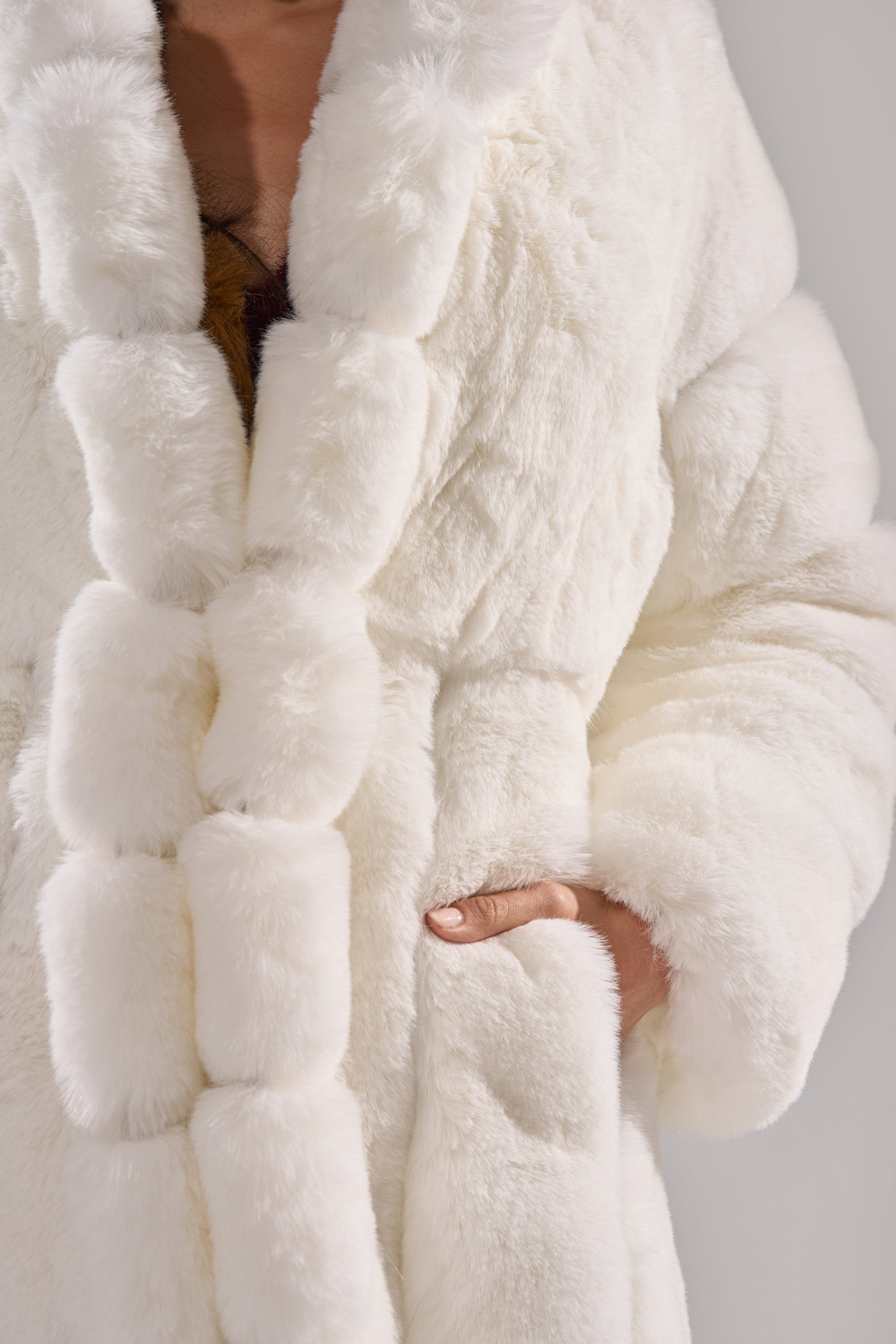 A person wearing the BERLIN HOODED FAUX FUR IN WHITE, with one hand in a side pocket. The plush faux fur looks irresistibly soft. Image is cropped to show only the torso and hand.