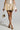 Dazzling in a short metallic gold dress with a flared skirt, they hold a small gold purse and wear AZALEA WANG BESSIE Brown Multi Snake Wedge Sandals. The understated light gray backdrop enhances their shimmering look.