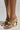 Close-up of a person wearing AZALEA WANG BESSIE brown multi snake wedge sandals with decorative chains and unique hollow wedge heels. Made from faux leather, these sandals feature two front straps and are displayed on a light background.