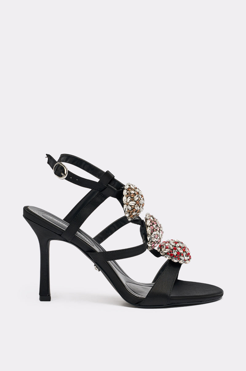 The AZALEA WANG BEST BLACK RHINESTONE EMBELLISHED STILETTO SANDAL features three gemstone embellishments in gold, silver, and pink on the front straps and a buckle ankle strap.