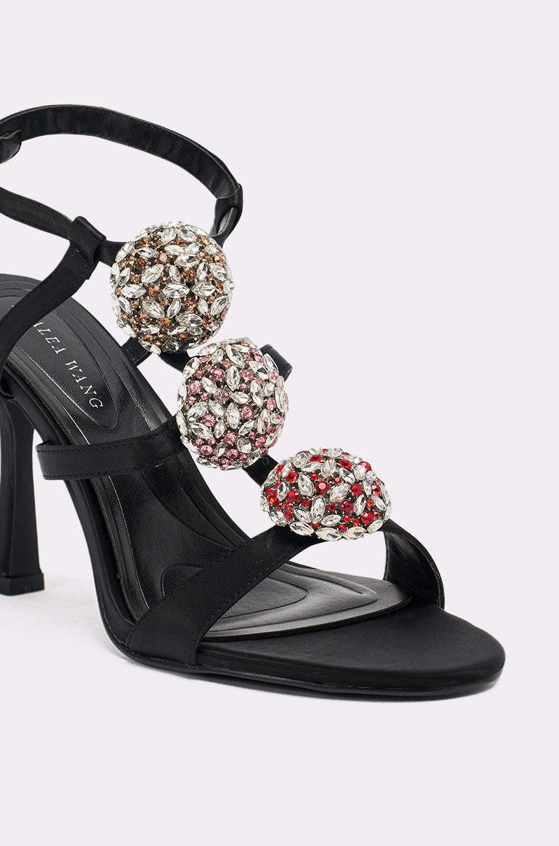 The AZALEA WANG BEST BLACK RHINESTONE EMBELLISHED STILETTO SANDAL features three large jeweled spheres in gold, silver, and red on its straps, shown against a white background.