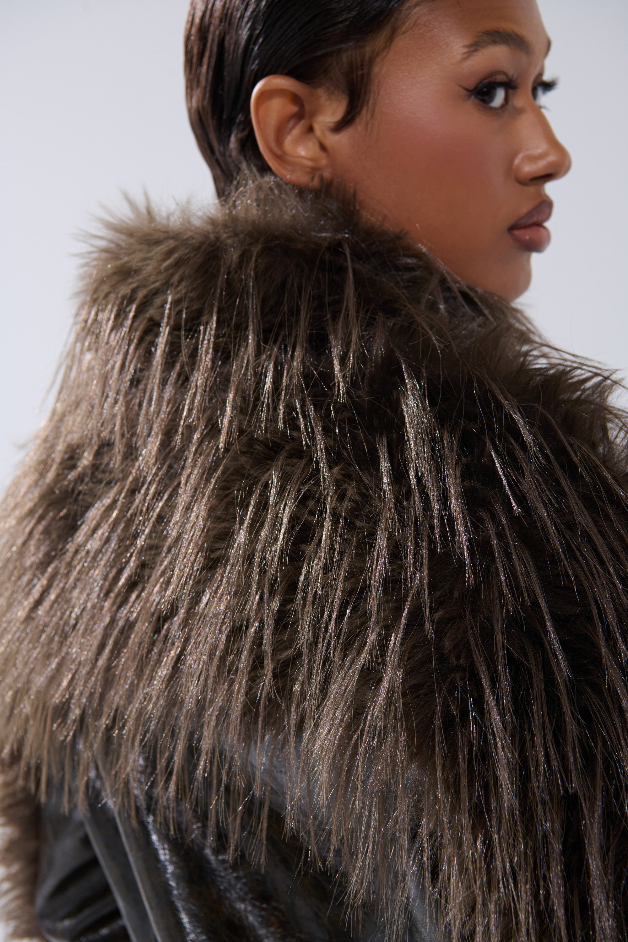 A person with short, slicked-back hair models the VOODOO FUR TRIM MOTO jacket—a dark faux leather moto with a prominent fur collar—while looking to the side against a neutral background.