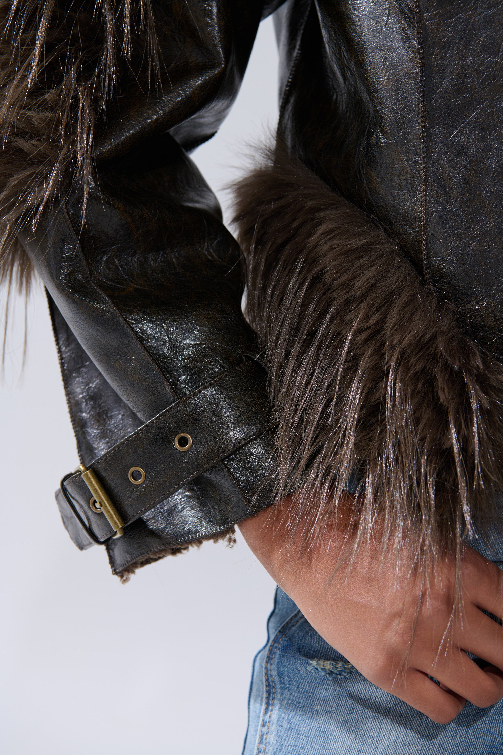 Close-up of a person wearing the VOODOO FUR TRIM MOTO jacket with brown fur trim on the cuffs and hem, paired with blue jeans, and one hand resting on their hip.