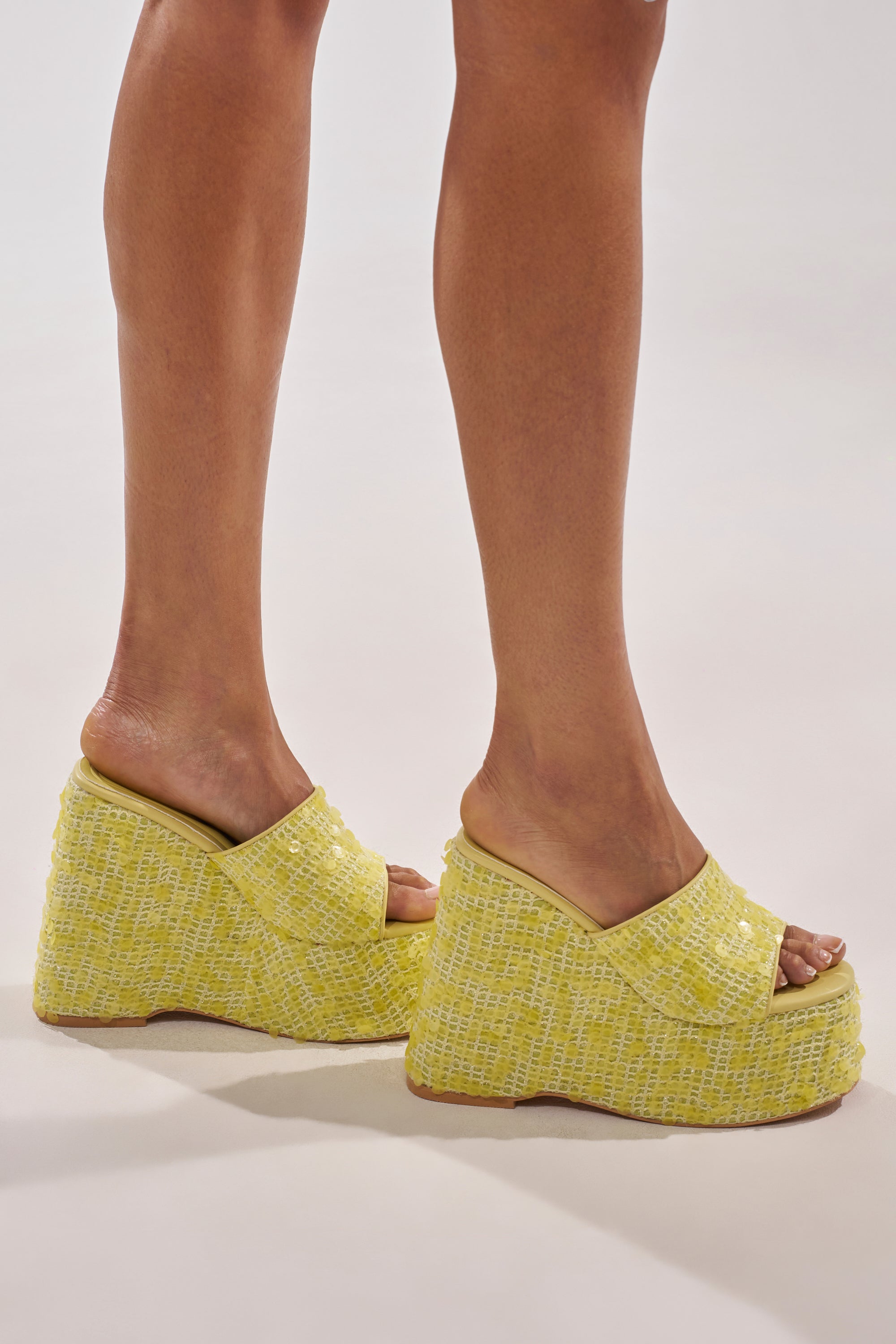 A person stands in AZALEA WANG BETSEY YELLOW SEQUIN RAFFIA WEDGE sandals featuring a woven platform, open toes, and slip-on design, shown from the side against a plain light background. 2