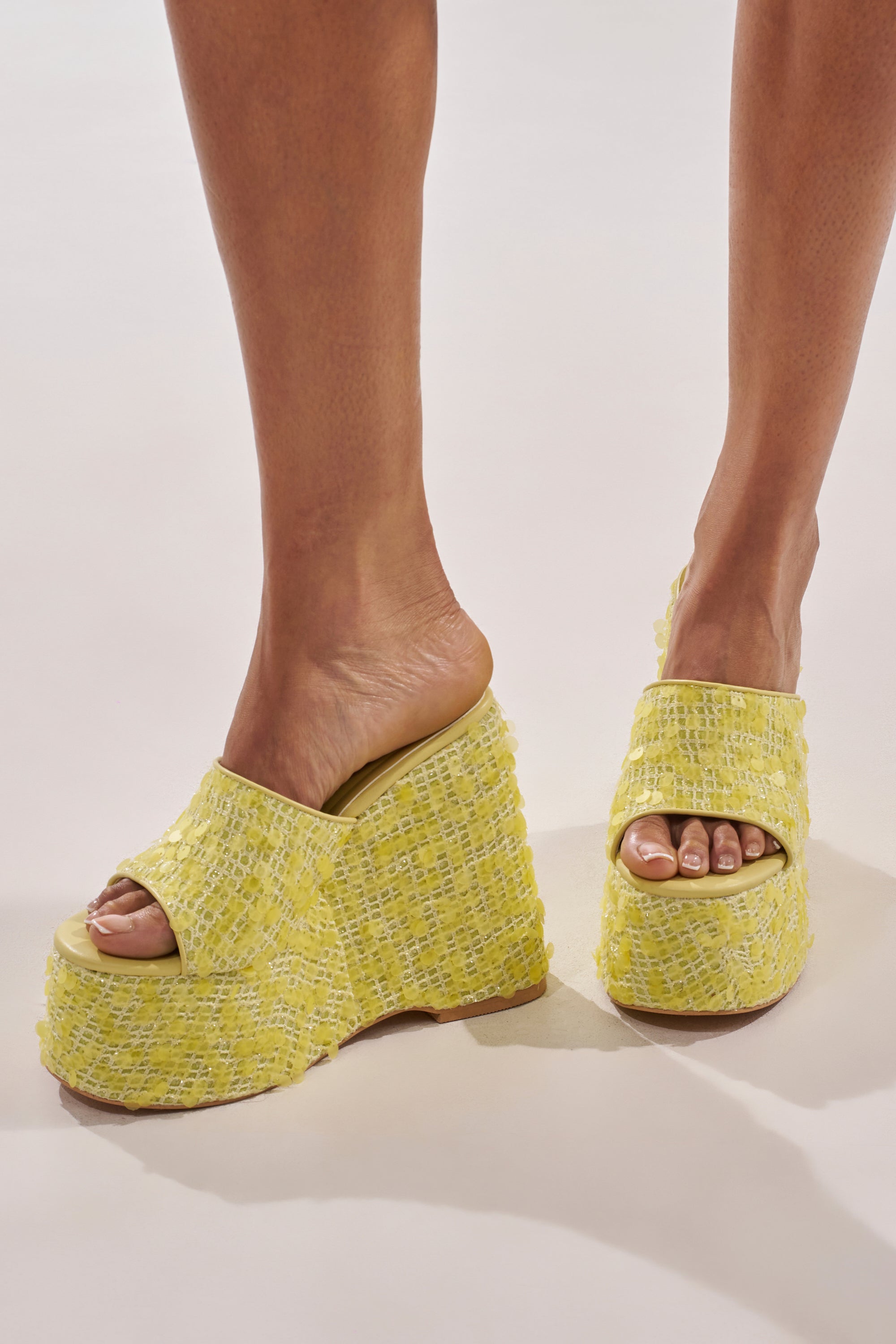 A person wears the AZALEA WANG BETSEY YELLOW SEQUIN RAFFIA WEDGE sandals—bright yellow, textured, open-toe and heel platform wedges—while standing on a light-colored surface. 3