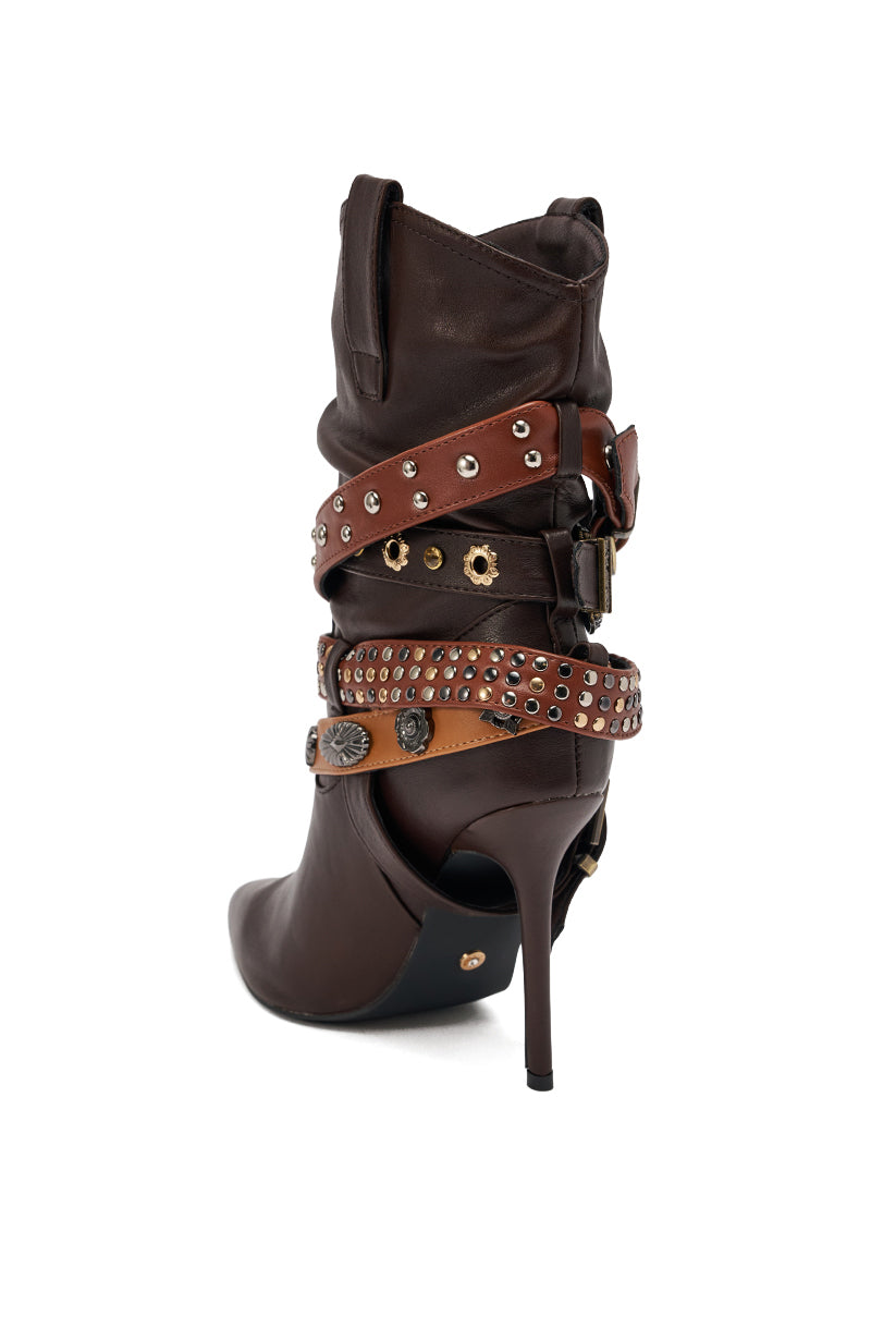 The AZALEA WANG BROWN STILETTO BOOTIE is a dark brown, high-heeled western bootie with a slouchy shaft, decorated with multiple brown and tan leather straps, metal studs, and buckles, shown on a white background.
