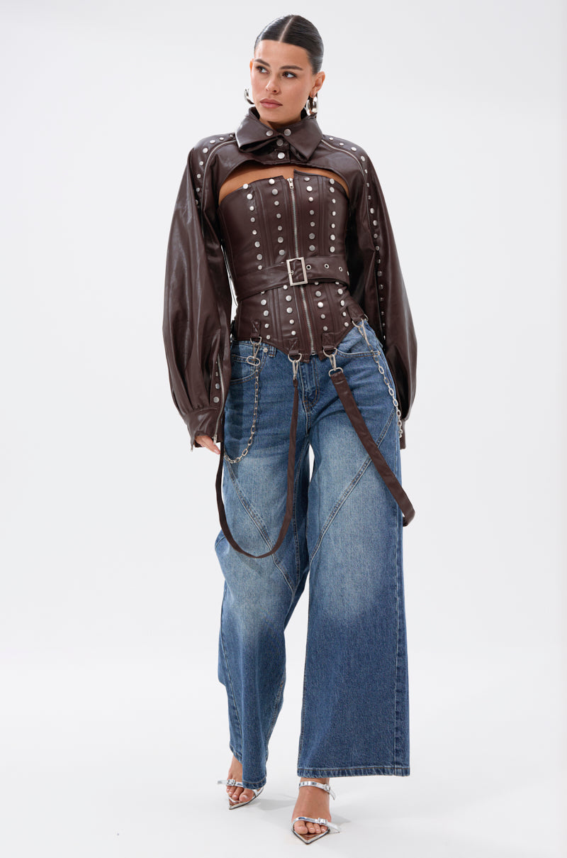 A person wears the PERK UP EMBELLISHED CORSET over a matching puffed-sleeve shirt, styled with wide-leg blue jeans featuring chains and silver heeled sandals, posing against a plain white background.
