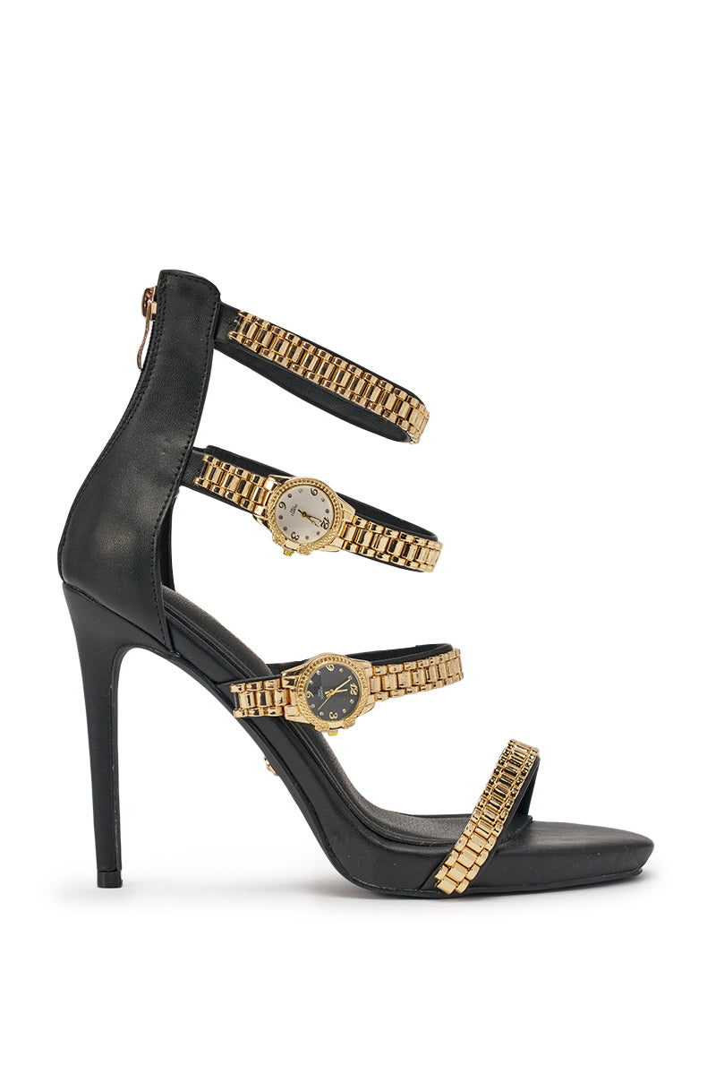The AZALEA WANG BEZEL WATCH STRAP NOVELTY STILETTO SANDAL is a black faux leather heel with three gold-tone watch-link straps, each adorned with a watch face, creating a stylish fusion of watch and stiletto design. 3