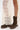 A person wearing a sheer, cream lace skirt and the AZALEA WANG BHARTI BROWN FLAT BOOTIE stands on a white background.