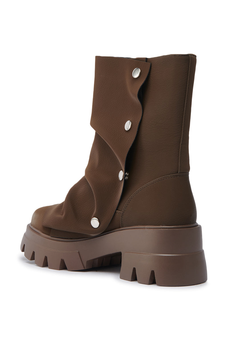 The AZALEA WANG BHARTI BROWN FLAT BOOTIE is a brown, mid-calf boot with a lug sole and layered faux leather flap with four silver snap buttons, shown from an angled rear view on a white background. 8