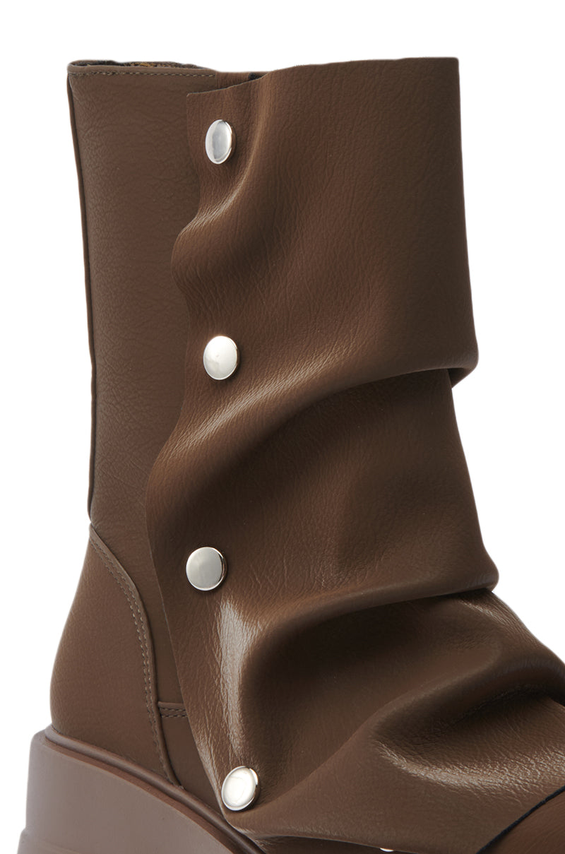 A close-up of the AZALEA WANG BHARTI BROWN FLAT BOOTIE, featuring brown faux leather, a slouched design, and four silver snap buttons along the outer side above a chunky heel. 9