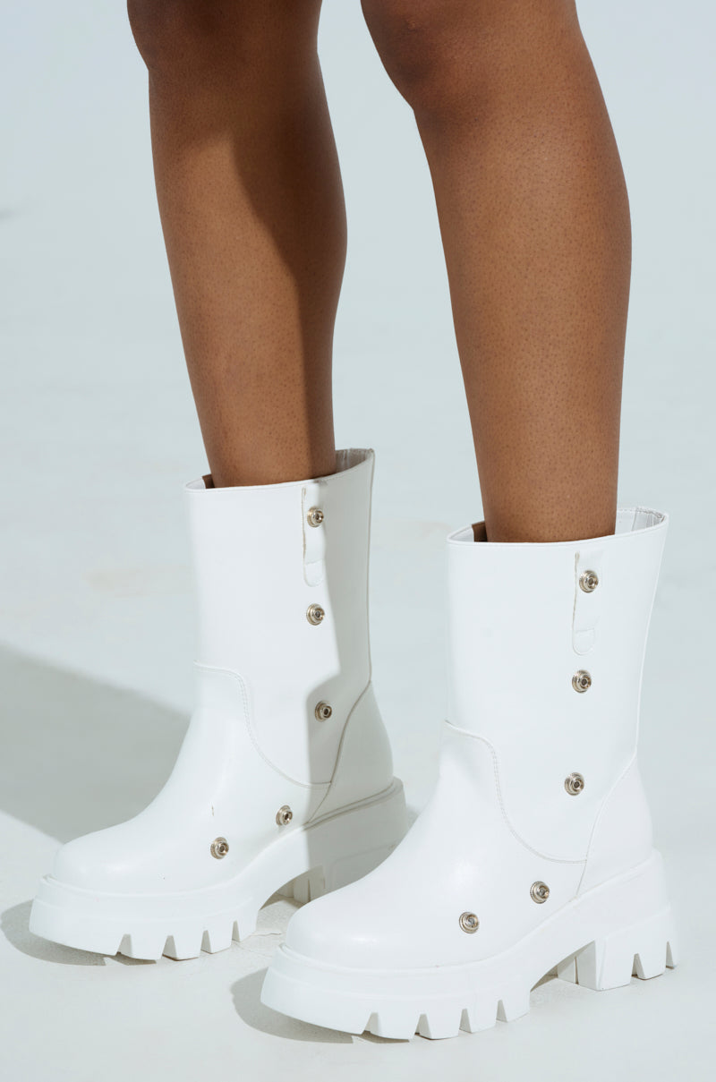 Close-up of someone wearing the AZALEA WANG BHARTI WHITE SNAP BOOTIE, featuring white vegan leather with metallic buttons and chunky heels, standing on a light surface. These mid-calf booties reveal the person's skin above them.