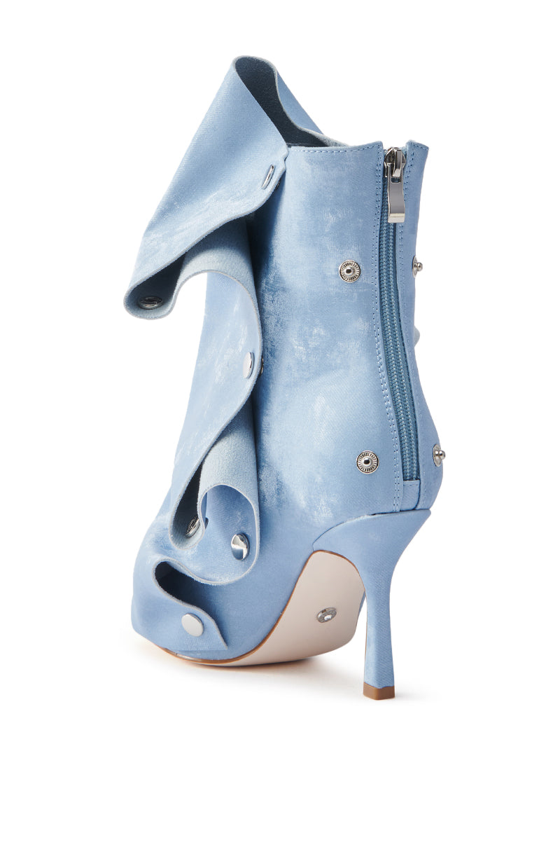 The AZALEA WANG BIRD SONG SNAP OPEN TOE BOOTIE IN BLUE is a stylish light blue heeled ankle boot with a textile upper, swirling ruffle design, metallic button accents, pointed toe, sleek stiletto heel, and side zipper closure.