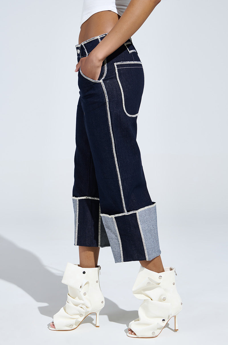A person in dark denim culottes and a white crop top poses against a plain white background, wearing the AZALEA WANG BIRD SONG SNAP OPEN TOE BOOTIE IN BONE, featuring faux leather stiletto heels, ankle-high design with button details.