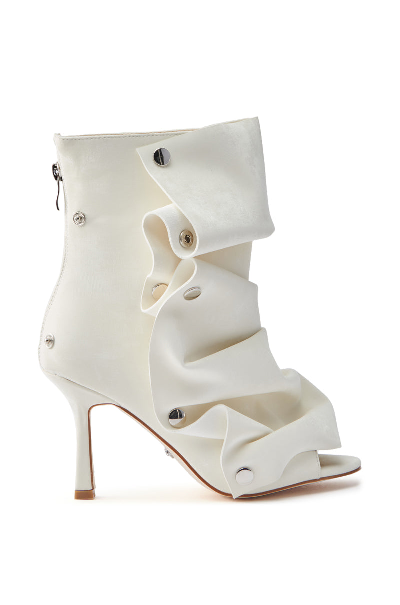 The AZALEA WANG BIRD SONG SNAP OPEN TOE BOOTIE IN BONE is a white faux leather ankle bootie with a distinctive ruffled design and metallic button accents, complete with a back zipper and slender heel.