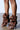 The AZALEA WANG BIRD SONG BROWN SNAP DETAIL OPEN TOE BOOTIE features brown leather and a unique scrunched design with button details, worn by a person standing on a concrete floor.
