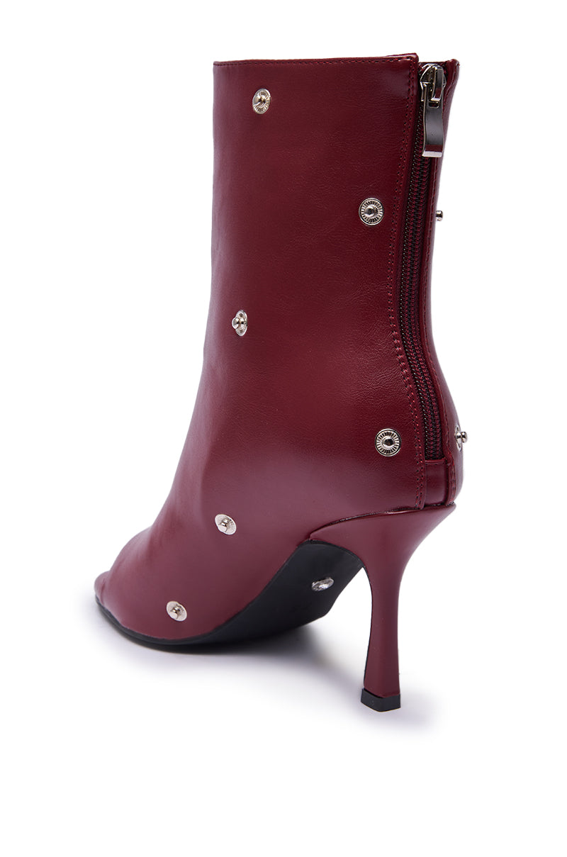 The AZALEA WANG BIRDSONG BURGUNDY SNAP OPEN TOE STILETTO BOOTIE, featuring metallic studs and a side zipper, is displayed from the back right angle against a white background.